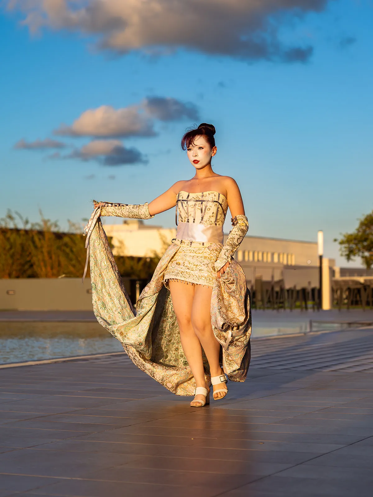 Model in gold-brocade gown and chain glove · sweeping skirt with the wind · rooftop pool and horizon at golden hour · Fashion Society UCF